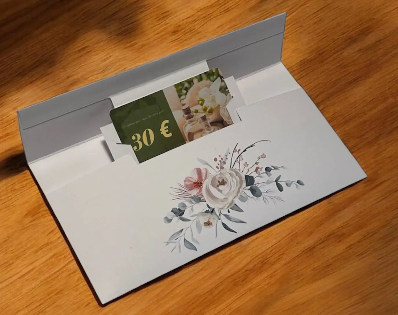 Pochette cadeau ou étui élégant blanc avec illustration florale, photo et carte cadeau 30 € visibles à l’intérieur.